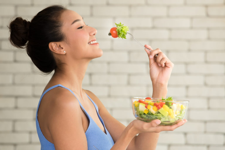 Asian woman in joyful postures with salad bowl on the side