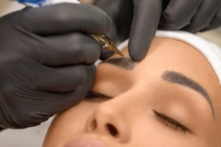 Beautiful young woman receiving microblading treatment on eyebrows