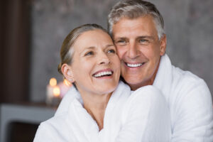 Smiling husband embracing cheerful wife from behind at medical spa for anti-aging treatments.